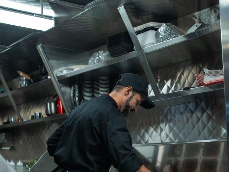 A worker cleaning stainless steel shelving in a commercial kitchen.